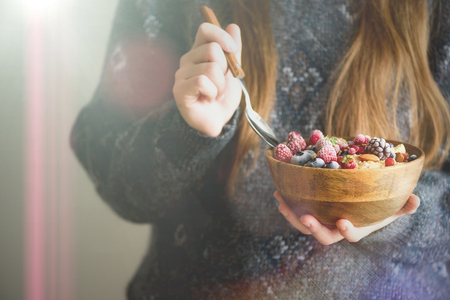 Woman hands holding oatmeal porridge with frozen berries, almonds in wooden bowl. Banner. Healthy breakfast. Clean eating, detox diet. Vegetarian, raw, vegan conceptの写真素材