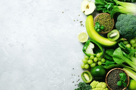 Organic green vegetables and fruits on grey background. Copy space, flat lay, top view. Green apple, zucchini, cucumber, avocado, kale, lime, kiwi, grapes, banana, broccoli, marbled lentils, mung bean.の写真素材