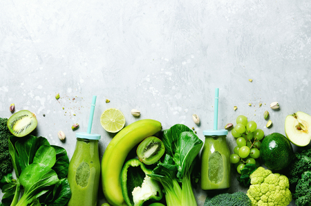 Green smoothie in glass jar with fresh organic green vegetables and fruits on grey background. Spring diet, healthy raw vegetarian, vegan concept, detox breakfast, alkaline clean eating. Copy space.の写真素材