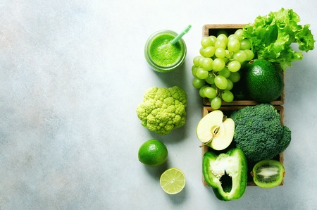 Green smoothie in glass jar with fresh organic green vegetables and fruits on grey background. Spring diet, healthy raw vegetarian, vegan concept, detox breakfast, alkaline clean eating. Copy space.の写真素材