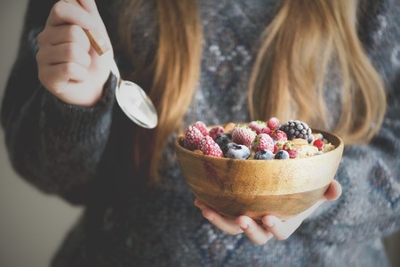 Girl hands holding oatmeal porridge with frozen berries, almonds in wooden bowl. Healthy breakfast. Clean eating, detox diet. Vegetarian, raw, vegan conceptの写真素材