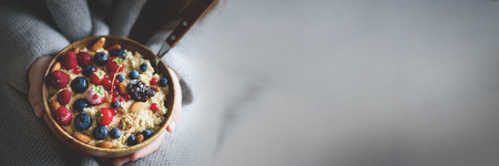 Girl hands holding oatmeal porridge with frozen berries, almonds in wooden bowl. Healthy breakfast. Clean eating, detox diet. Vegetarian, raw, vegan conceptの写真素材