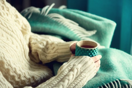 Woman's hand in woolen sweater holding cup of tea with lemon on a cold day. Copy space. Winter and Christmas holidays conceptの写真素材