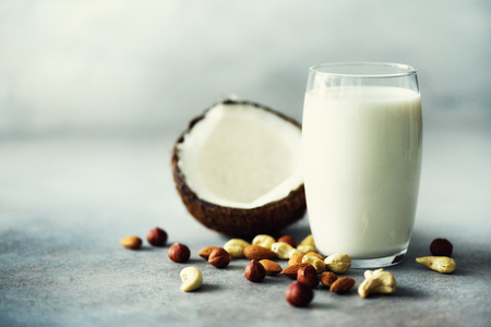 Organic vegan nut milk in glass with various assortment of nuts - coconut, almond, cashew, hazelnut on grey concrete background, copy space. Banner.の写真素材