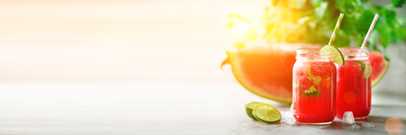 Fresh red watermelon slice and smoothie in glass jar with straw, ice, mint, lime on light background, copy space, sunlight. Banner.の写真素材