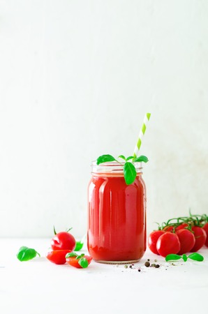 Organic fresh tomato juice in a glass jar, basil, cherry, salt, pepper and straw on light background. Clean eating and diet concept. Copy spaceの写真素材