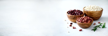 Various of kidney beans. Red, white and black kidney beans in wooden bowls with rosemary on grey concrete background. Copy space, banner.の写真素材
