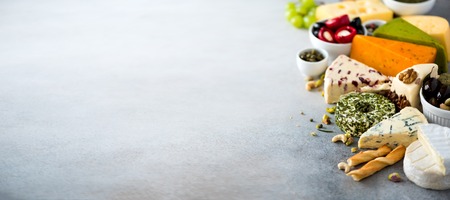 Assortment of hard, semi-soft and soft cheeses with olives, grissini bread sticks, capers, grape, on...