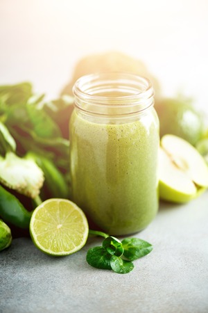 Glass jar mugs with green health smoothie, kale leaves, lime, apple, kiwi, grapes, banana, avocado, lettuce. Copy space, sunlight effect. Raw, vegan, vegetarian, detox, alkaline food concept.の写真素材