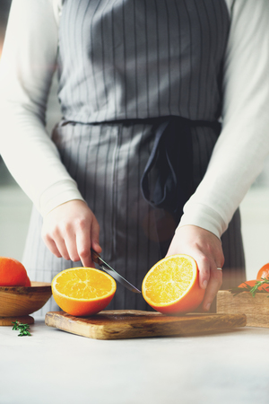 Woman hands slicing orange, cutting citrus fruit. Knife, wooden cutting board on design white kitchen. Copy spaceの写真素材