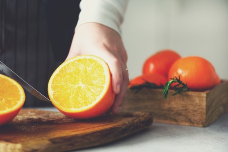 Woman hands slicing orange, cutting citrus fruit. Knife, wooden cutting board on design white kitchen. Copy spaceの写真素材