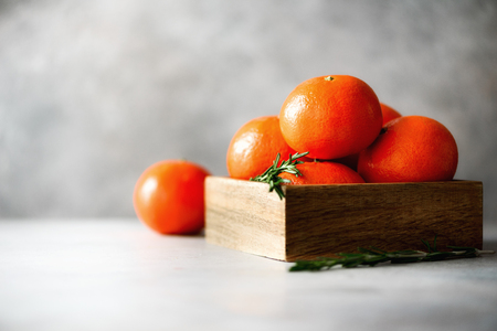 Orange tangerines, mandarins, clementines, citrus fruits with rosemary in wooden box on grey concrepe background, copy space.の写真素材