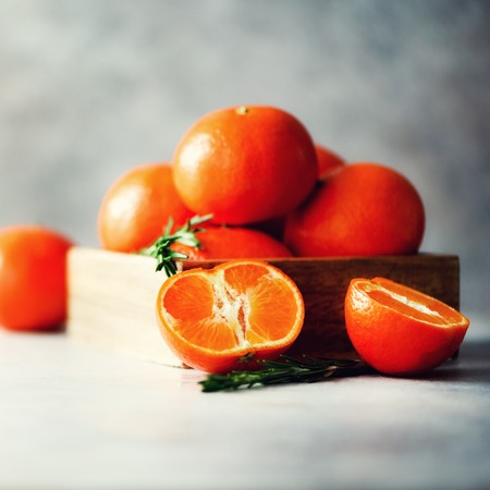 Orange tangerines, mandarins, clementines, citrus fruits with rosemary in wooden box on grey concrepe background, copy space.の写真素材