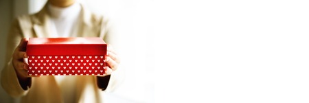 Female hands holding red gift box with white hearts, copy space. Christmas, hew year, birthday, valentines day concept. Bannerの写真素材