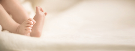 Newborn baby feet on creamy blanket. Mom and her child. Maternity, family, birth concept. Copy space for your text. Banner.の写真素材