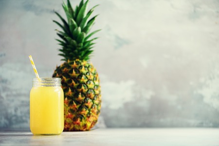 Glass bottle of pineapple juice and whole fruit on gray background with copy space. Summer, holiday concept. Raw, vegan, vegetarian, clean eating diet.の写真素材