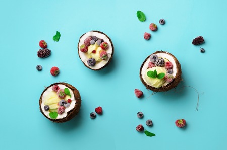 Coconut ice cream with fresh berries in coconuts halves on blue background with copy space. Top...