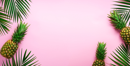 Pineapples and tropical palm leaves on punchy pastel pink background. Summer concept. Creative flat lay with copy space. Top view.の写真素材