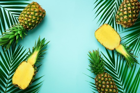 Pineapples and tropical palm leaves on punchy pastel turquoise background. Summer concept. Creative...