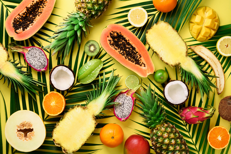 Exotic fruits and tropical palm leaves on pastel yellow background - papaya, mango, pineapple, banana, carambola, dragon fruit, kiwi, lemon, orange, melon, coconut, lime. Top viewの写真素材