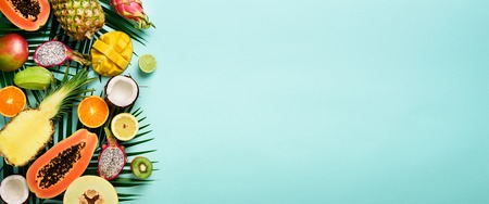 Exotic fruits and tropical palm leaves on pastel turquoise background - papaya, mango, pineapple, banana, carambola, dragon fruit, kiwi, lemon, orange, melon, coconut, lime. Banner. Top viewの写真素材