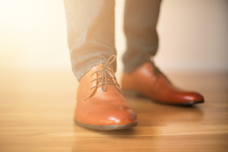 Man wearing shoes on wooden floor. Clothing concept, groom getting ready before ceremony. Body detail of businessman. Sunlight bokehの写真素材