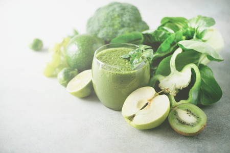 Glass with green health smoothie, kale leaves, lime, apple, kiwi, grapes, banana, avocado, lettuce. Sunlight bokeh. Copy space. Raw, vegan, vegetarian, alkaline food conceptの写真素材