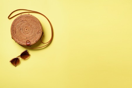 Round rattan bag, sunglasses on yellow background. Banner. Top view with copy space. Trendy bamboo bag and white shoes. Summer fashion flat lay. Trip, vacation conceptの写真素材