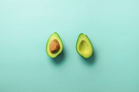 Green avocado halves with seed on blue pastel background. Creative minimal flat lay style with copy space. Summer food concept. Top view. Pop art design.の写真素材