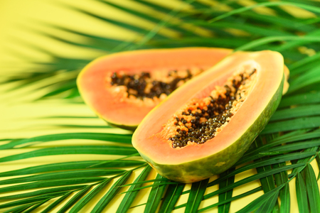 Exotic papaya fruit over tropical green palm leaves on yellow background. Copy space. Pop art design, creative summer concept. Raw vegan food.の写真素材