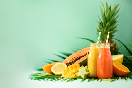 Juicy papaya and pineapple, mango, orange fruit smoothie in two jars on turquoise background. Detox,...