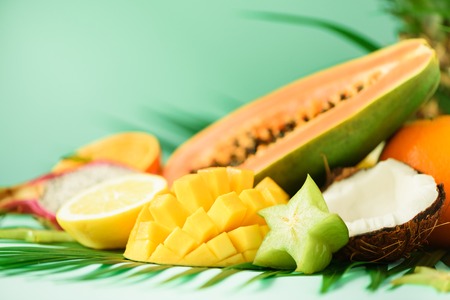 Assortment of exotic fruits on turquoise background. Detox, vegan food, summer concept. Papaya, mango, pineapple, carambola, dragon fruit, kiwi, orange, melon, coconut, lime over palm leaves.の写真素材