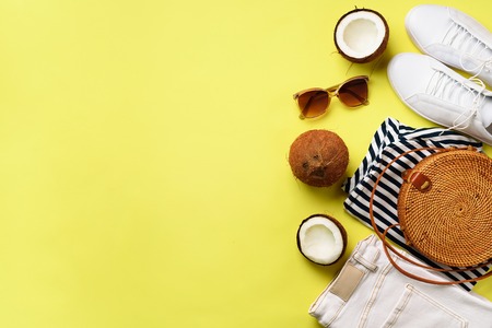 Female white sneakers, jeans, striped t-shirt, rattan bag, coconut and sunglasses on yellow background with copy space. Top view. Summer fashion, capsule wardrobe concept. Creative flat lay.の写真素材