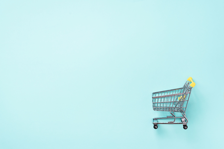 Shopping cart on blue background. Minimalism style. Creative design. Top view with copy space. Shop trolley at supermarket. Sale, discount, shopaholism concept. Consumer society trendの写真素材