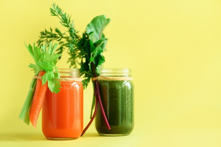 Healthy organic green and orange smoothies on yellow background. Detox drinks in glass jar from vegetables - carrot, celery, beet greens and tops. Copy space. Summer food concept.の写真素材