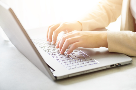 Close-up of hands typing on laptop keyboard at the office. Copy space. Worker, business, remote work, always connect, online banking concept. Soft focus. Sunlight bokeh effect.の写真素材