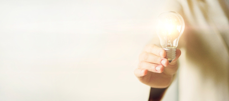 Woman hand holding light bulb on cream background with copy space. Creative idea, new business plan, motivation, innovation, inspiration conceptの写真素材