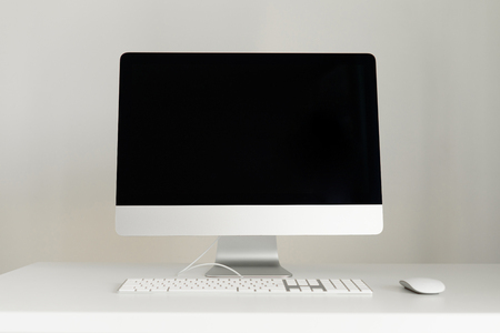 Keyboard, mouse, computer display with black blank screen. Front view. Designer workspace on grey background. Minimalistic home office. Copy space.の写真素材
