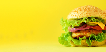 Macro view of tasty burger with beef, cheese, lettuce, onion, tomatoes on yellow background. Close up banner. Unhealthy diet concept and copy space.の写真素材