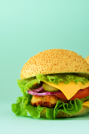 Macro view of tasty burger with beef, cheese, lettuce, onion, tomatoes on blue background. Close up banner. Unhealthy diet concept. Copy space.の写真素材
