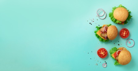 Fast food, unhealthy diet concept. Juicy homemade burgers, tomatoes, cheese, onion, cucumber and lettuce on blue background. Top view. Banner with copy spaceの写真素材