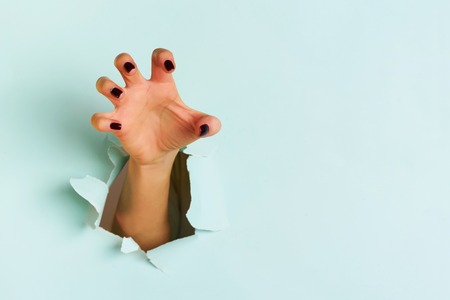 Female hand reaching through torn blue paper sheet.の写真素材