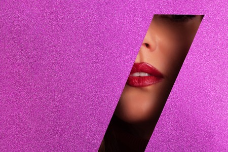 Girl with bright make up, red lipstick looking through hole in violet paper.の写真素材