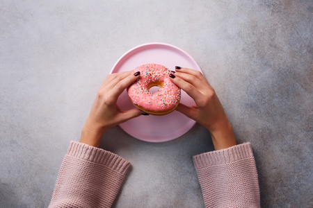Female hands holding donut on pink plate over stoneの写真素材
