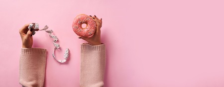 Female hands holding donut and measuring tape over pinkの写真素材