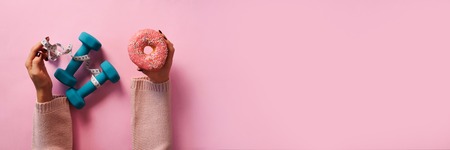Female hand holding sweet donut, measuring tape, dumbbells over pinkの写真素材