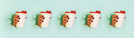 Pattern of female hand holding white paper mug on blue background. Take away coffee cup concept. Mock up with copy space.の写真素材