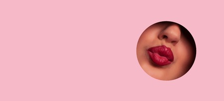 View of beautiful red lips giving kiss through hole in pink paperの写真素材
