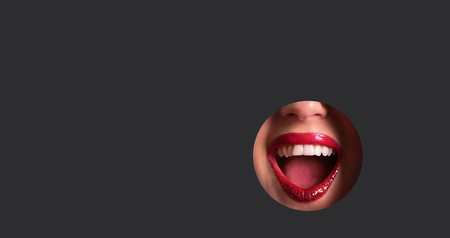 Red lips and shiny smile through hole in dark grey paperの写真素材