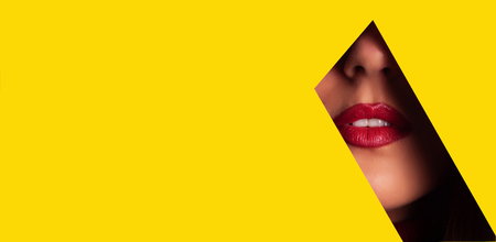 Girl with bright make up, red lipstick looking through hole in yellow paper.の写真素材